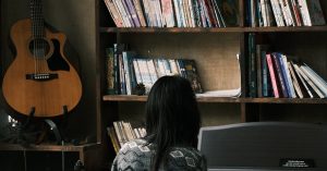 Person playing piano near bookshelf and guitar.